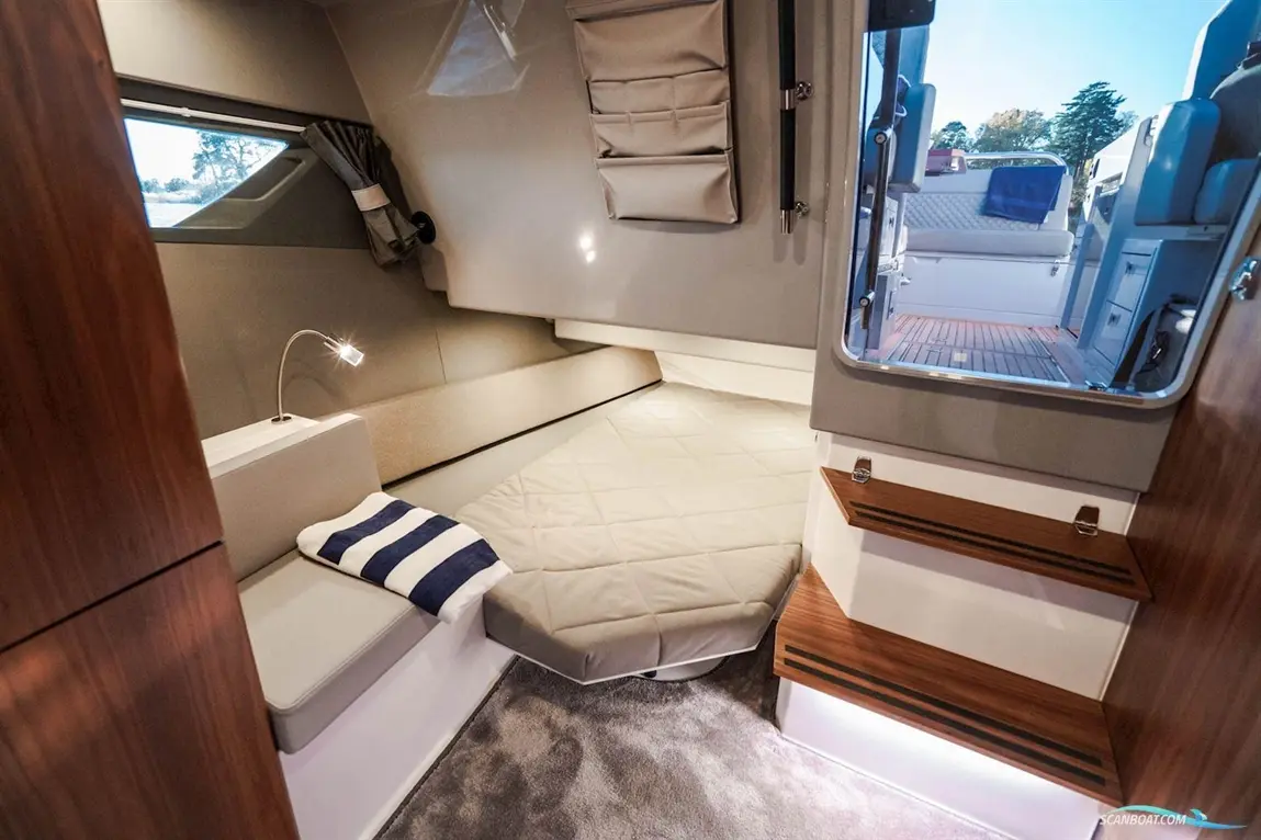 Modern boat interior featuring a seating area, a small bed, and steps leading to an outdoor deck, with a grey and beige colour scheme.